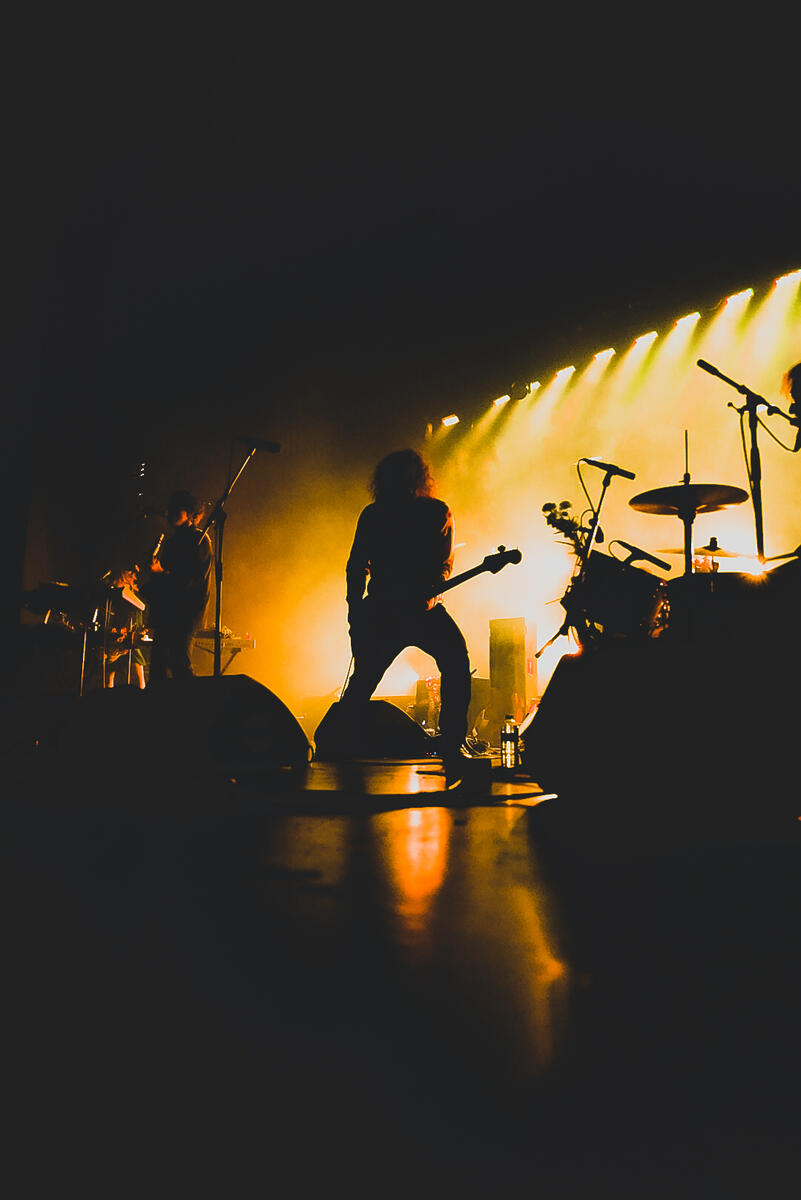 Color image of bassist playing on stage with orange yellow lights and fog. Band is "Born Ruffians""
