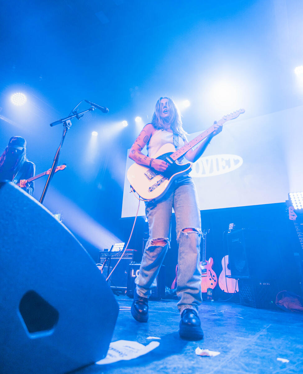 Colour photograph of lead vocalist walking and playing on stage. Wide angle. Band is "Loviet"