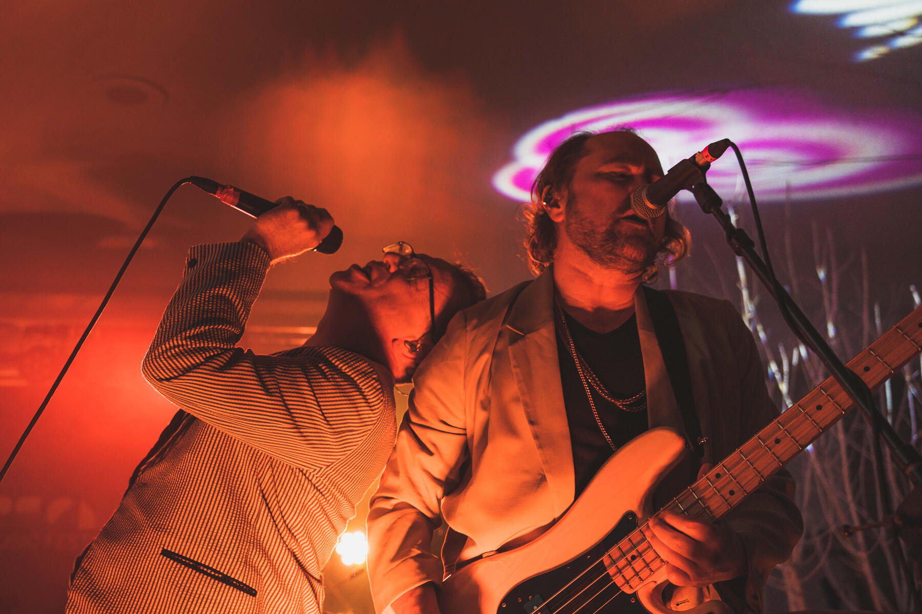 Close up color image of lead singer leaning and singing on shoulder of bassist and back up vocalist. Band is "Stars"