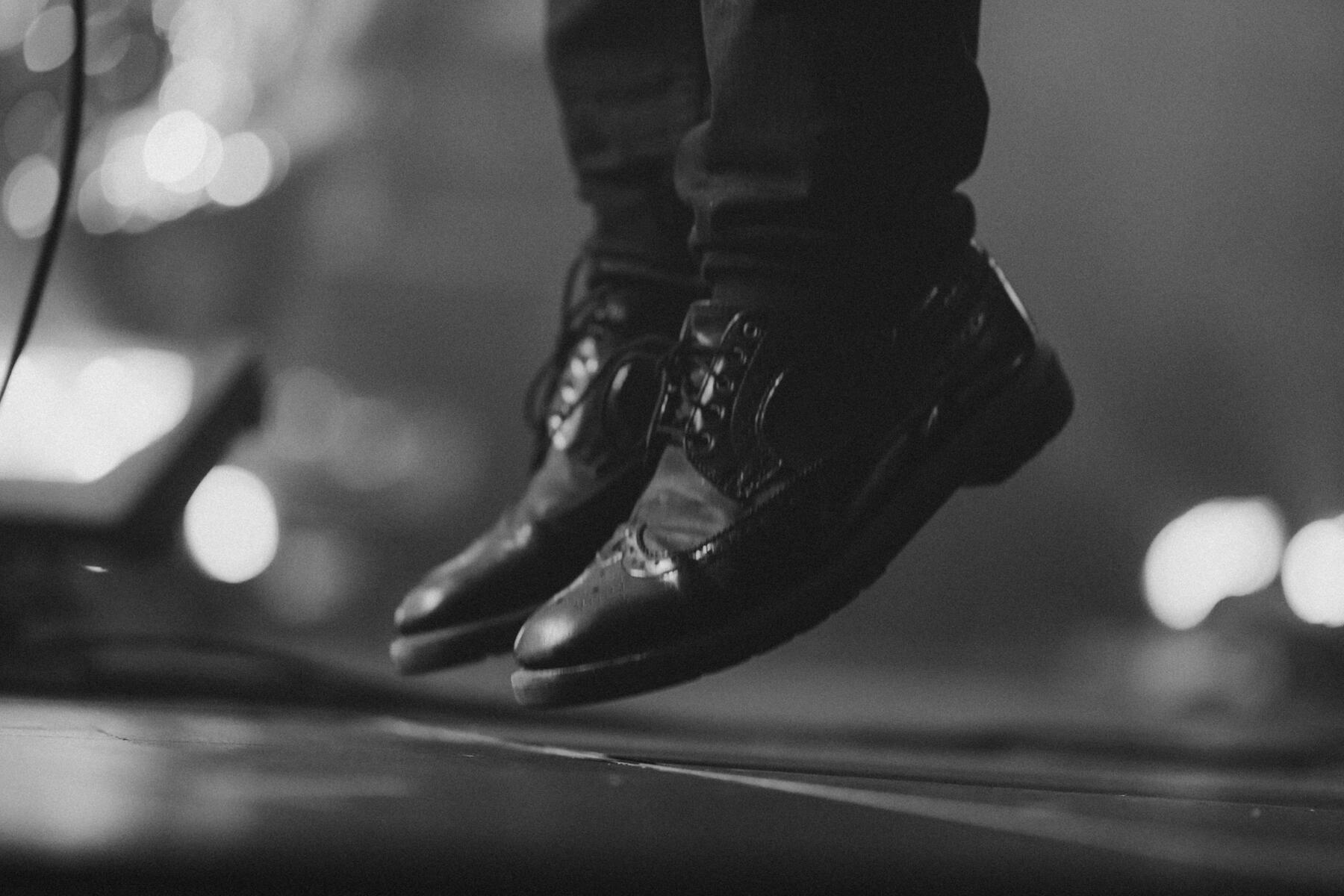 Black and white of band member&#39;s feet elevated of the stage in a jump. Band is &quot;Men Without Hats&quot;