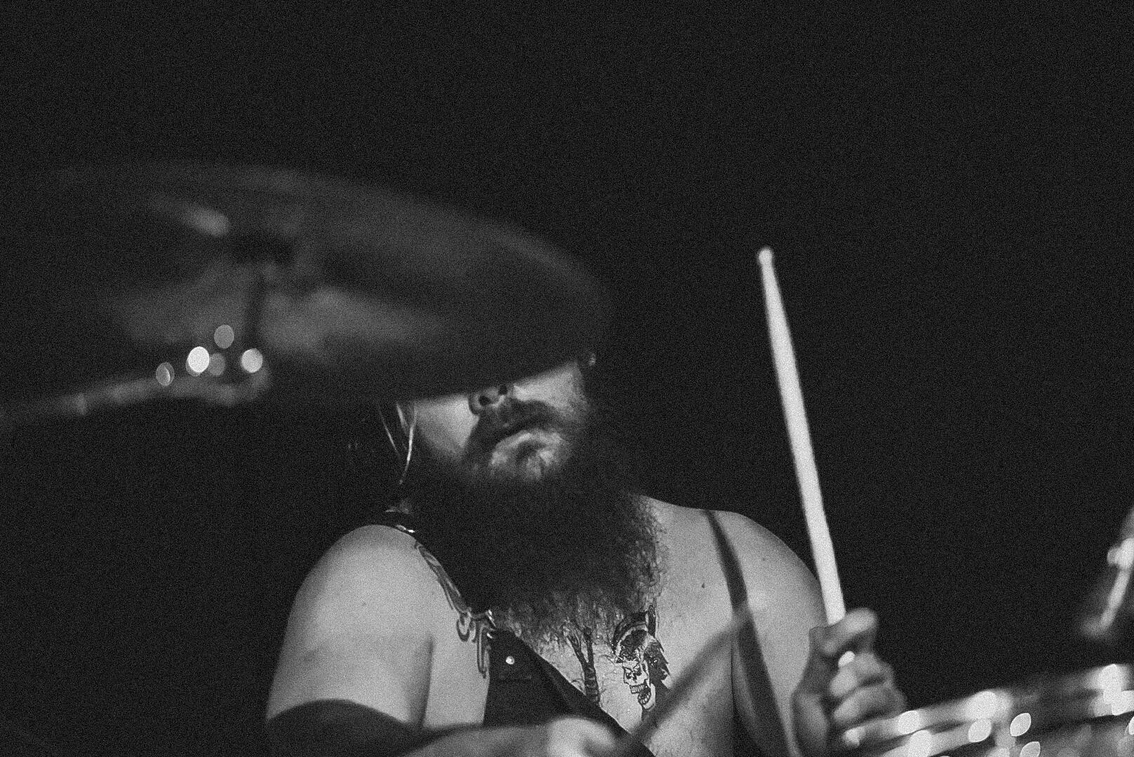 Black and white image of drummer with cymbal is covering their eyes. Band is &quot;El Paladin&quot;